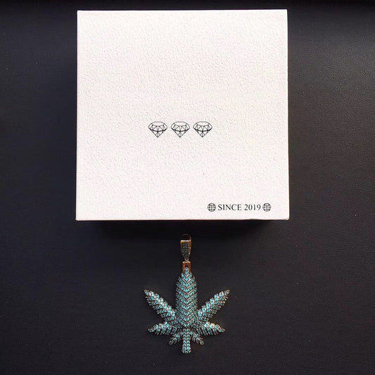 DatNewDrip iced out pot leaf pendant in green pave stones on gold bail displayed with white box