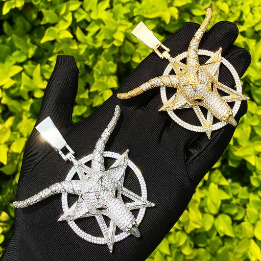 Two iced out goat pendant necklaces in silver and gold styles displayed on a hand against green foliage
