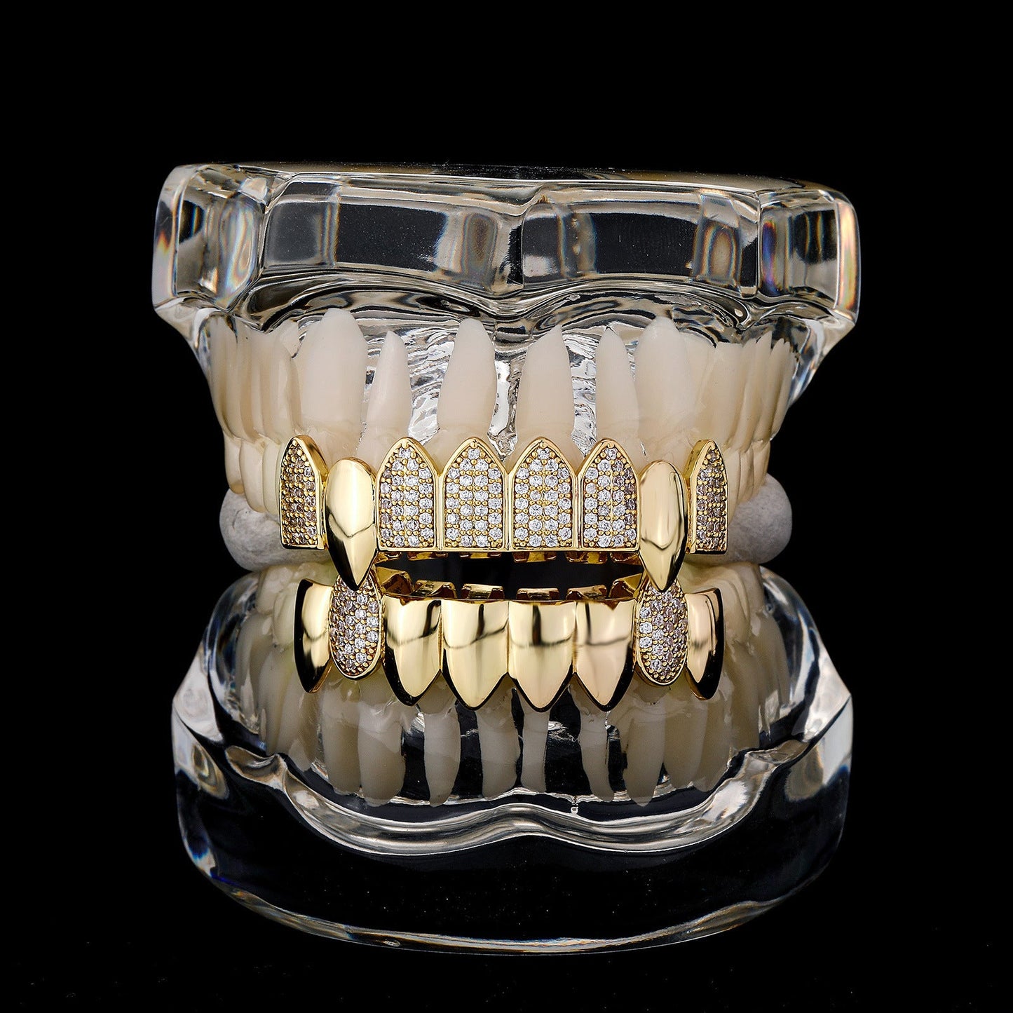 Clear dental model displaying gold iced out fang grillz with pave stones on upper and lower teeth