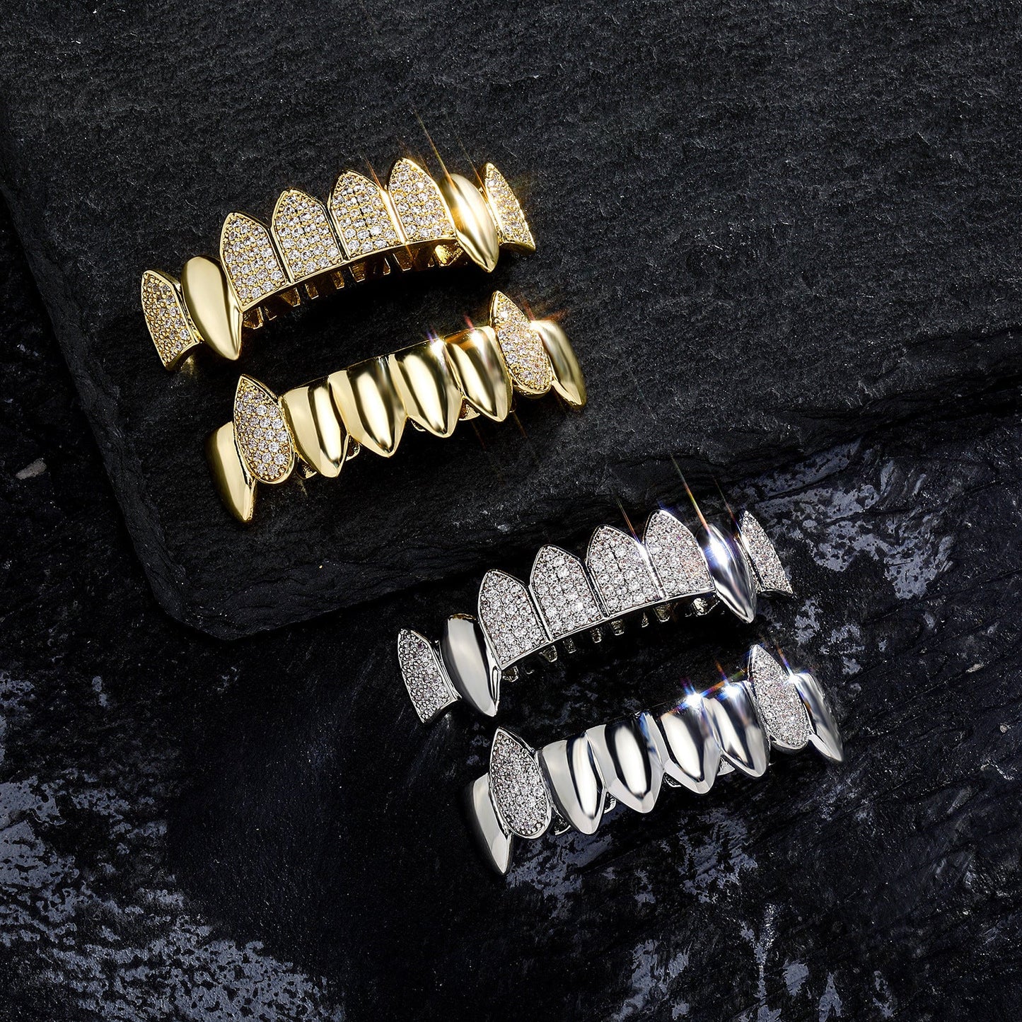 Gold and silver iced out fang grillz sets with pave stones displayed on black textured slate