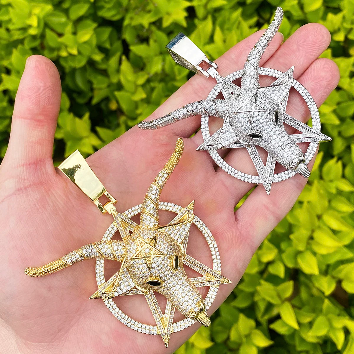 Iced out goat pendant necklace in gold and silver held in hand against a green background