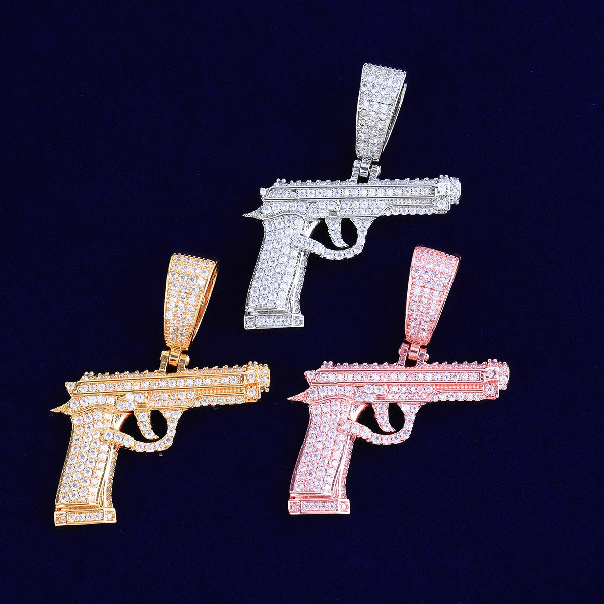 Three iced out gun necklaces in gold, silver, and rose gold featuring sparkling rhinestones