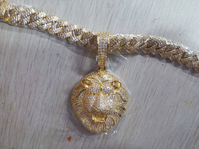 DatNewDrip gold iced out lion head pendant encrusted with clear stones on matching iced Cuban link chain